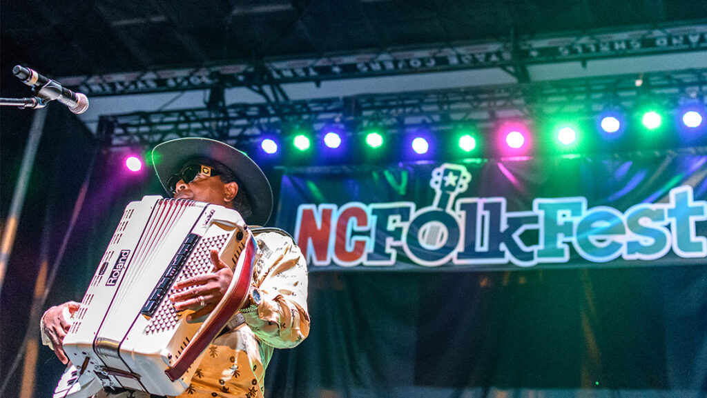 A musician plays an accordion onstage in front of the sign NC Folk Fest.