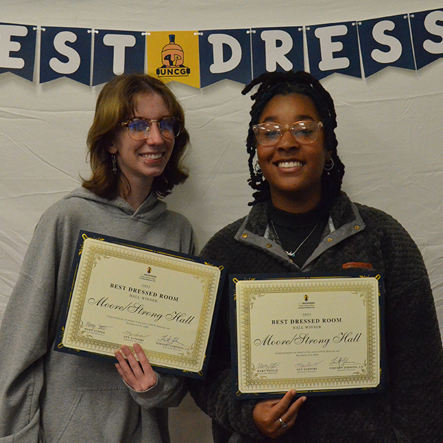 Two students stand with certificates in front of a banner that says "Best Dressed".