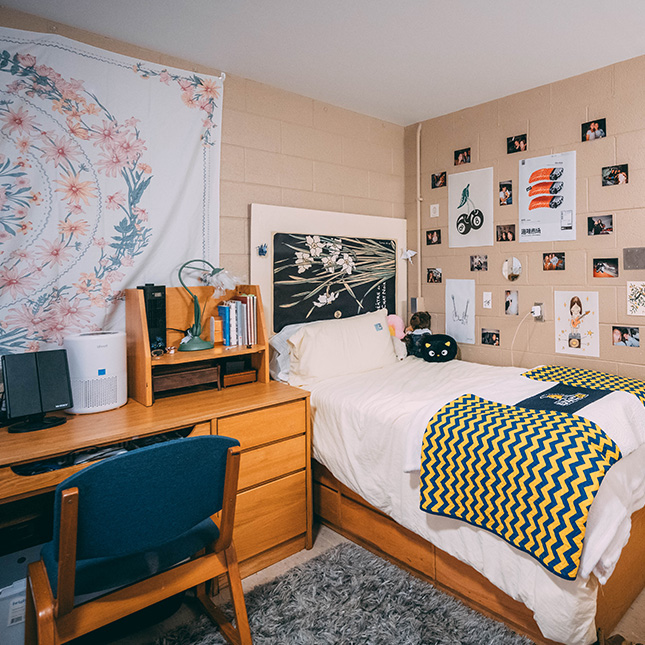 Dorm room with UNCG blanket on the bed, wall hangings and photos on the wall. 