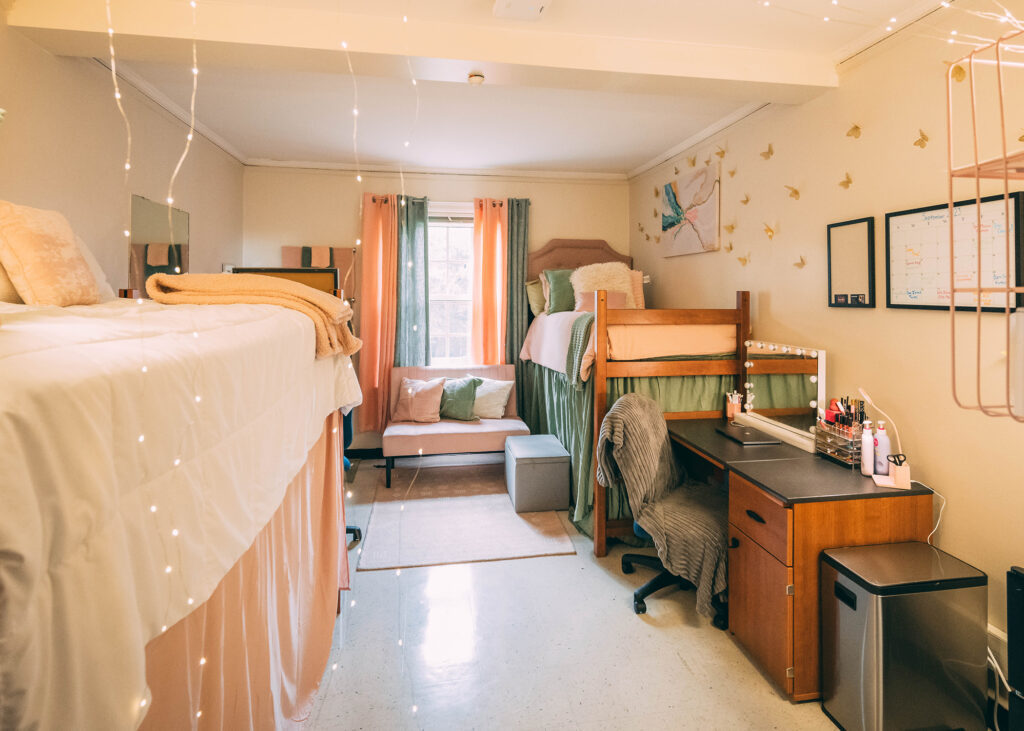 Dorm room decorated with raised beds and pink and green comforters and window treatments.