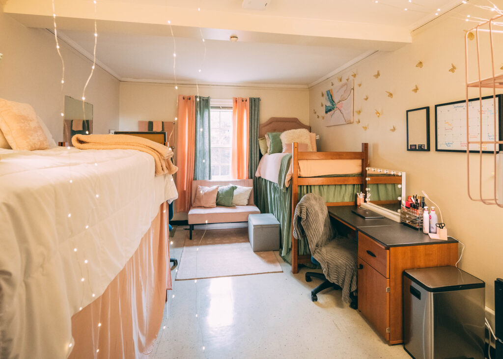 Dorm room decorated with raised beds and pink and green comforters and window treatments. 