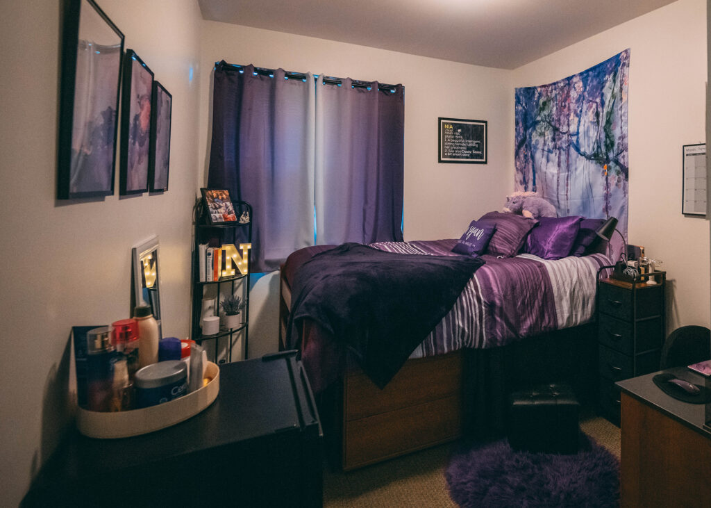 Dorm room decorated with purple bedding and accents. 