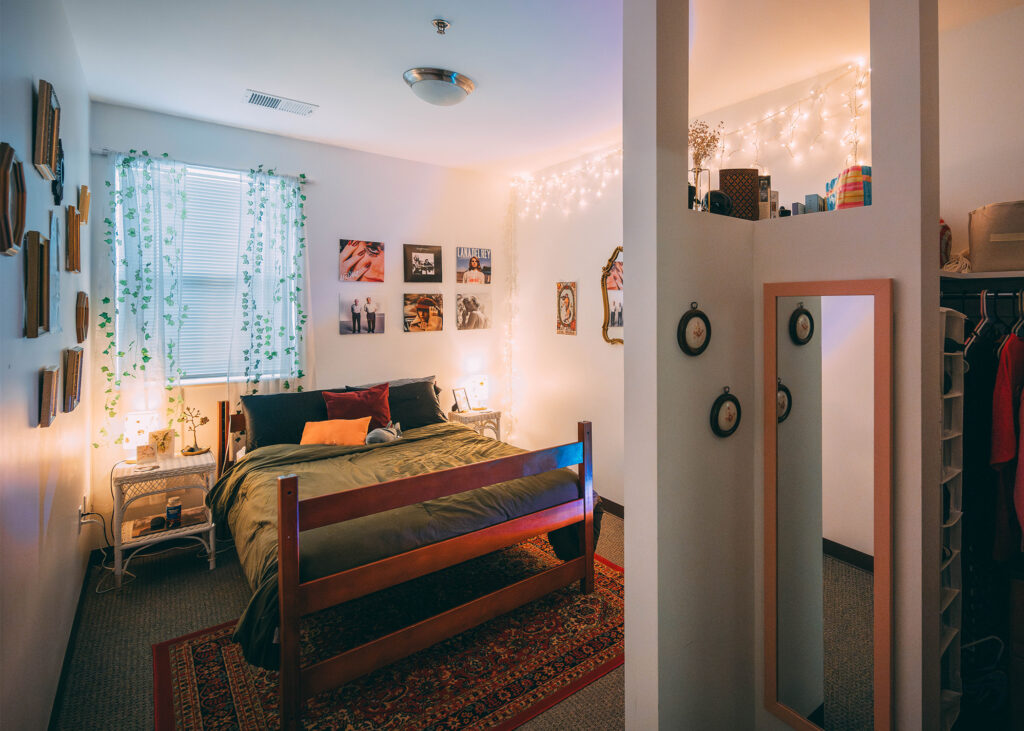 Dorm room decorated with a double bed, rug and framed pictures on the wall. 