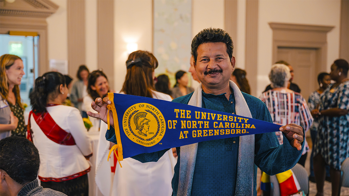 Fulbright TEA Scholar stands with UNCG pennant flag at the opening reception in September 2023.