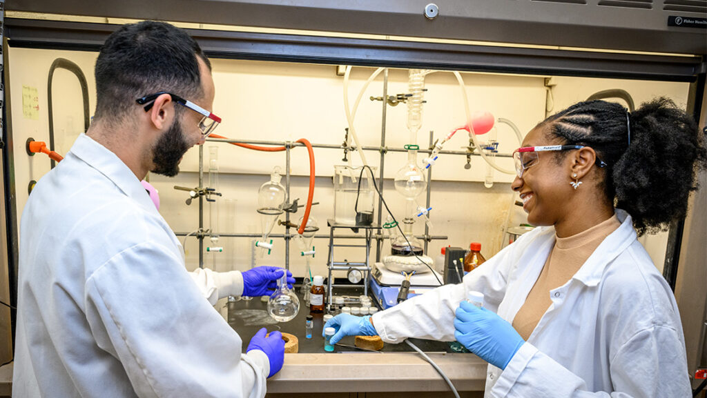 Two chemistry students in white lab coats in a lab.