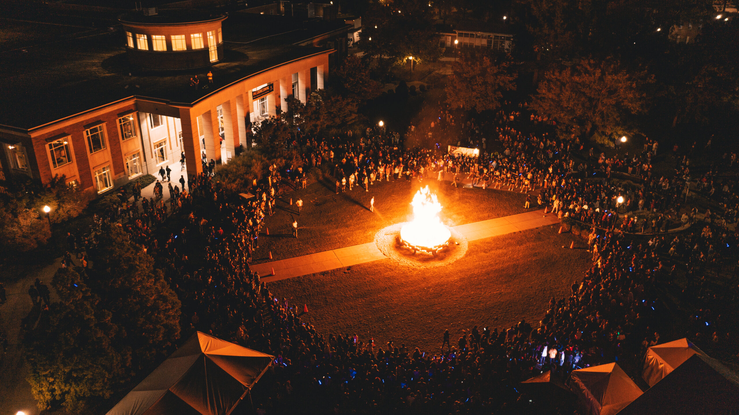 An aerial view of the homecoming bonfire surrounded by students on Kaplan Commons.