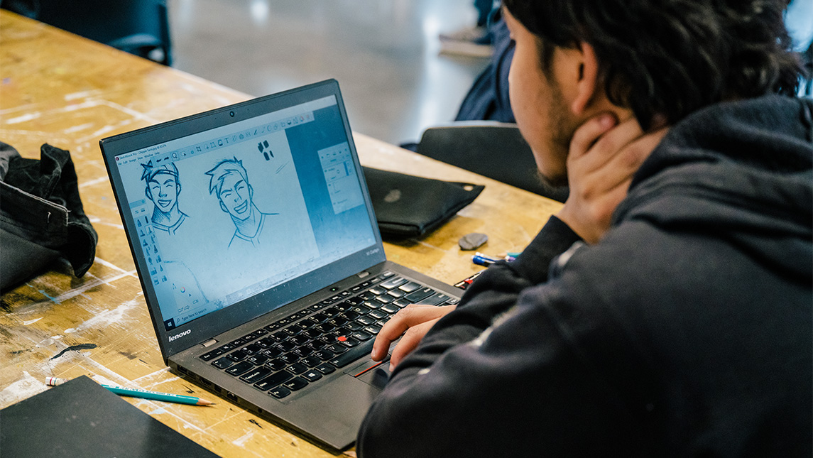 A UNCG student designs a cartoon character on his laptop.
