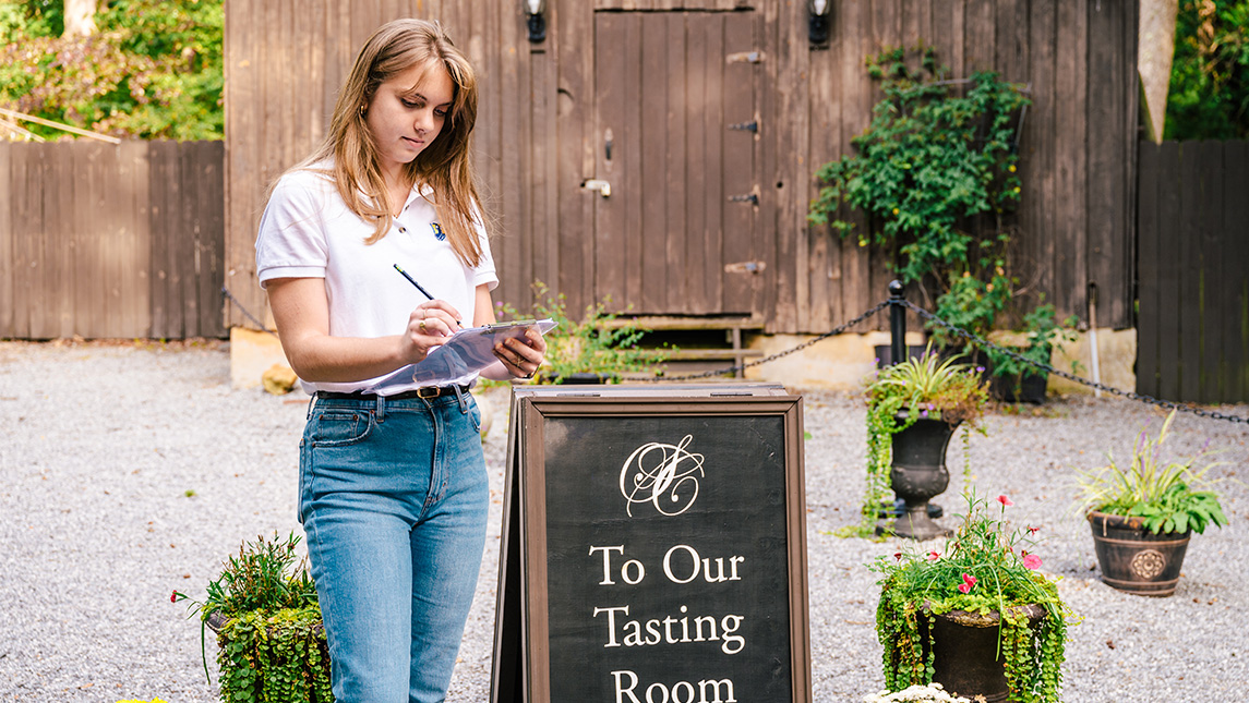 A UNCG student takes notes beside the sign to a wine tasting room.