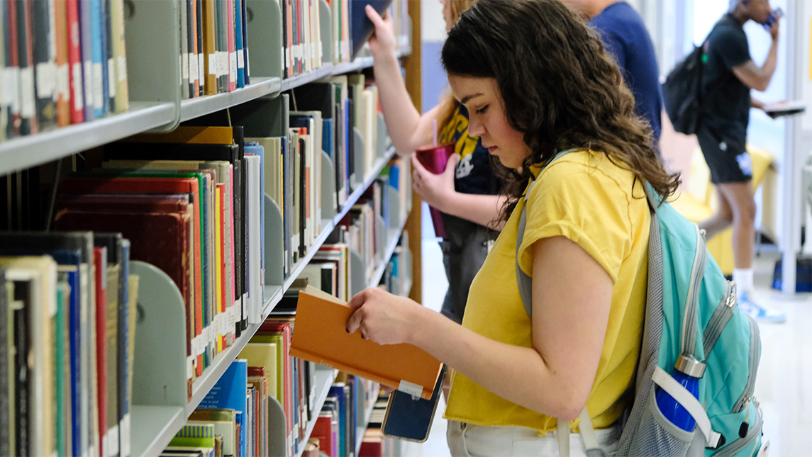 A student examines a book she took off the UNCG Jackson Library shelves.