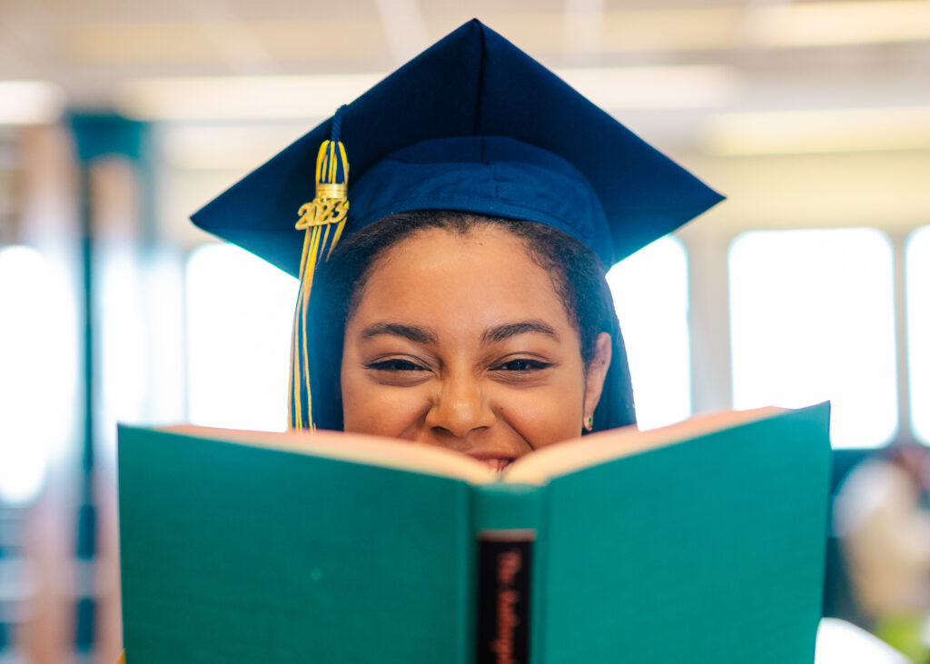 Girl in a graduation cap peers over an open book.