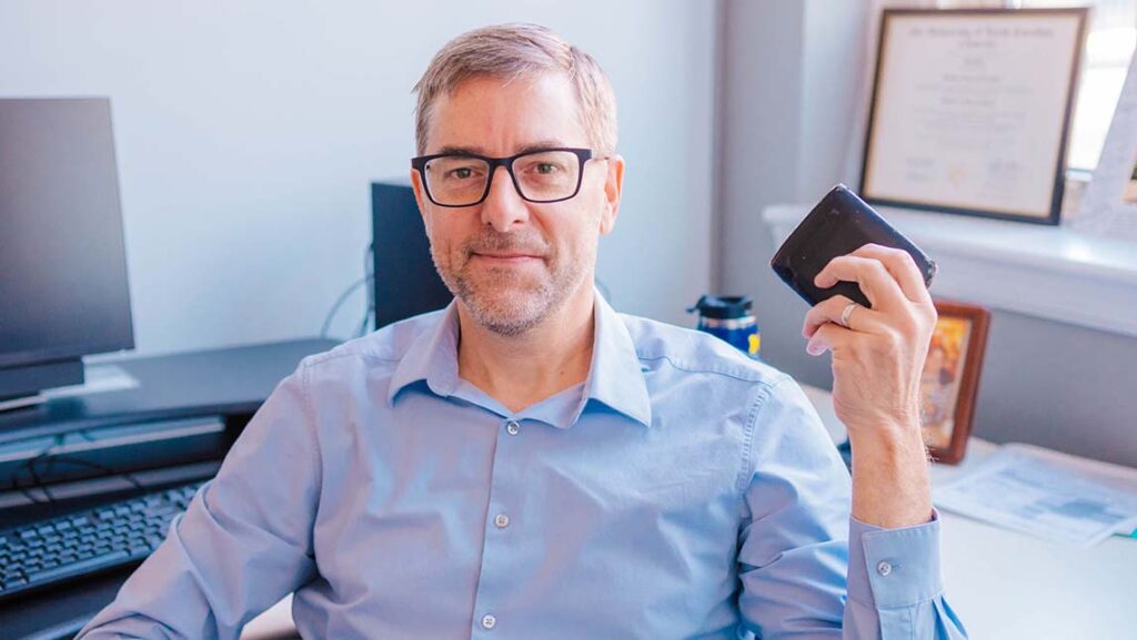 A man wearing glasses holds up his wallet.