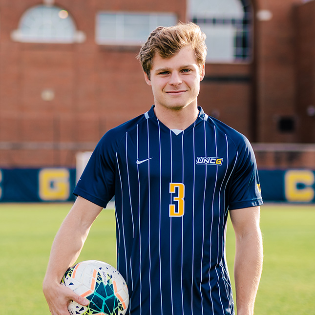 UNCG Men's soccer player stands with ball.