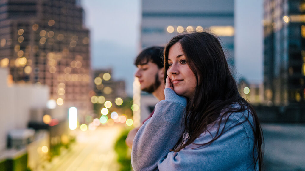 Two students gaze at the sunset from a parking garage in Greensboro with the downtown skyline in the background.
