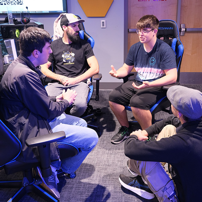 4 students group chairs together to work on a project in the esports arena.