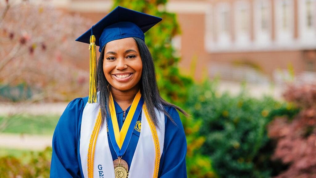 UNCG student Kemiah Williams stands in her cap and gown.