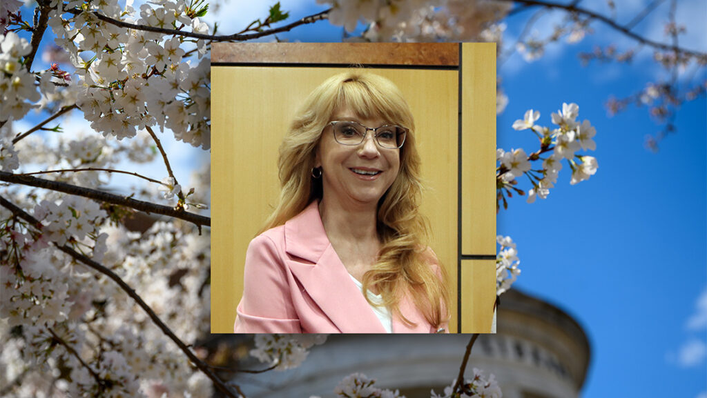 Photo of Kimberlianne Podlas against a backdrop of tree blossoms.