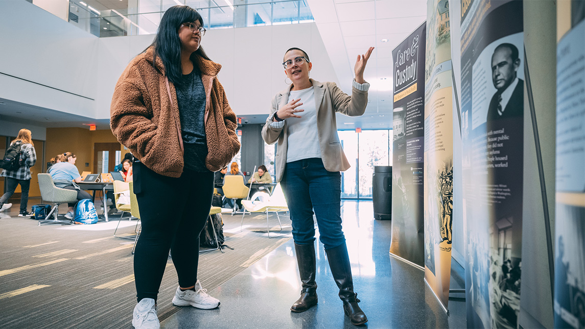 Two people stand in front of an exhibit in UNCG's Nursing Instructional Building.