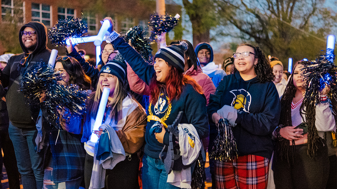 A crowd of UNCG students waves glow sticks as they walk down the street.