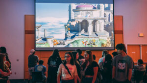 A large projection screen displays a Super Smash Bros. game in progress at UNCG.