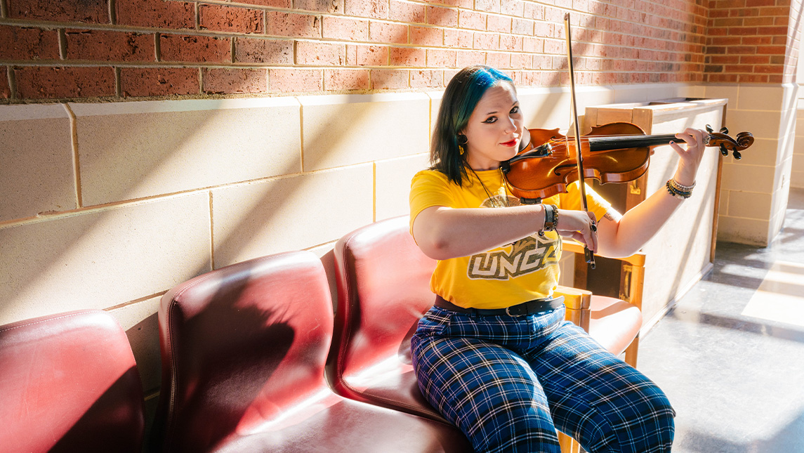 Elena Cousin plays violin while looking at the camera.