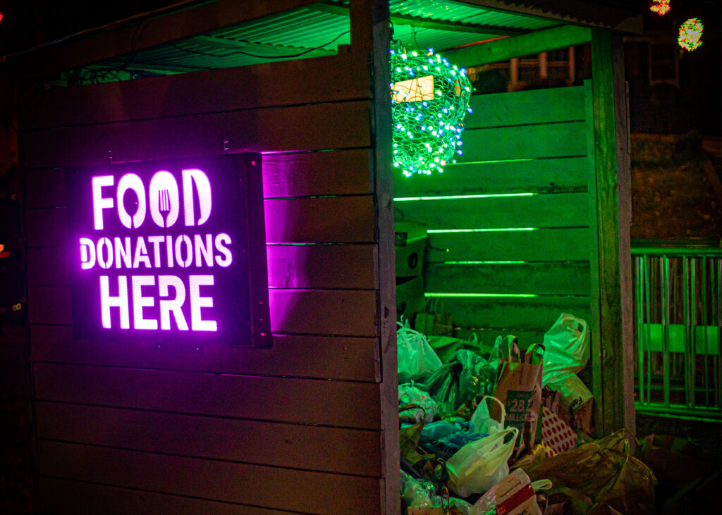 Wooden trailer full of grocery bags of canned goods with a lighted sign on the side that reads "Food Donations Here".