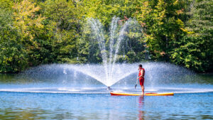 A UNCG student stands atop a paddleboard near the Piney Lake fountain.