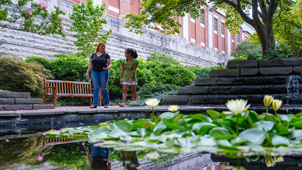 Two people walk past the pond outside UNCG's School of Music building.