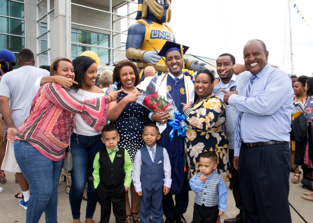 A family gathers around a graduate after commencement. Everyone points to the proud grad.