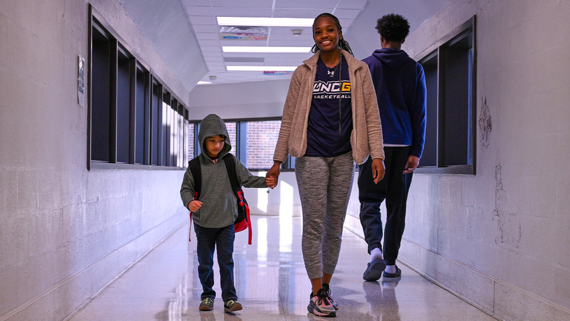 UNCG women’s basketball player Nia Howard walks with a child at Gateway Education Center