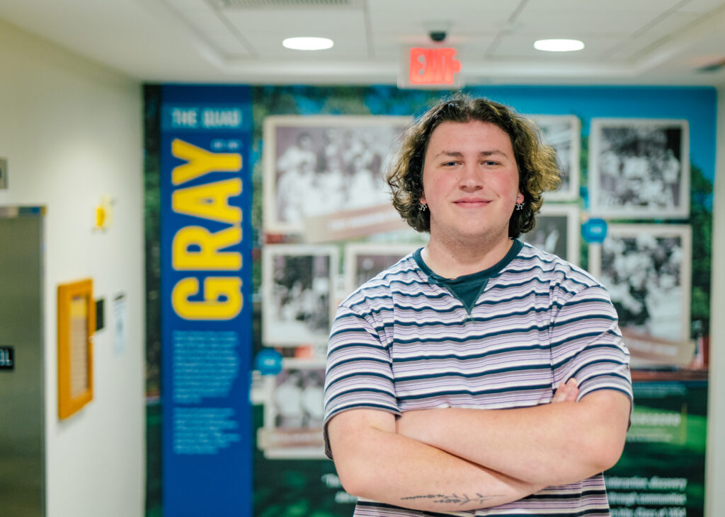 Student stands in a residence hall posing in front of a display screen.