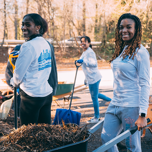 UNCG students in "Changemaker" shirts help to spread mulch at New Arrivals Institute.