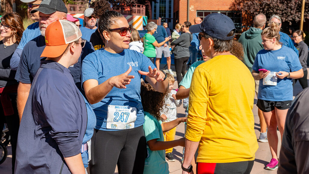 A woman in a blue shirt speaks with two other individuals wearing race bibs.