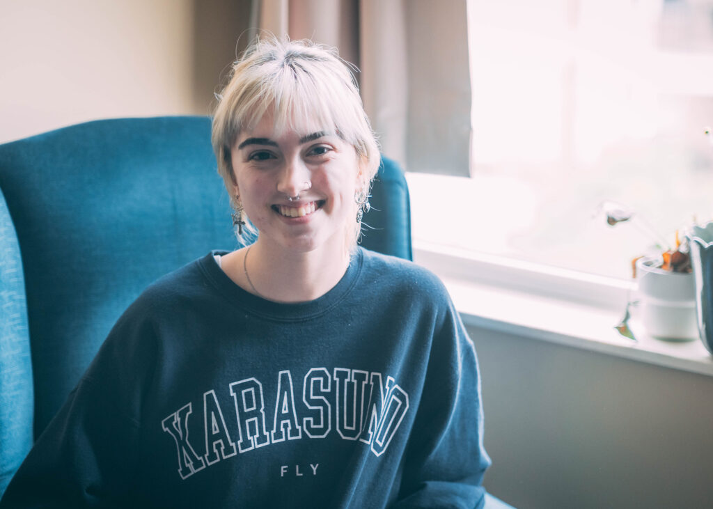 Student sits in a wingback chair in front of a window in her residence hall. 