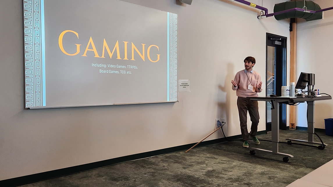 A man stands behind a desk as he gives a presentation about gaming.