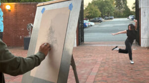 A UNCG art student does a sketch on an easel of a dance student performing in Weatherspoon courtyard.
