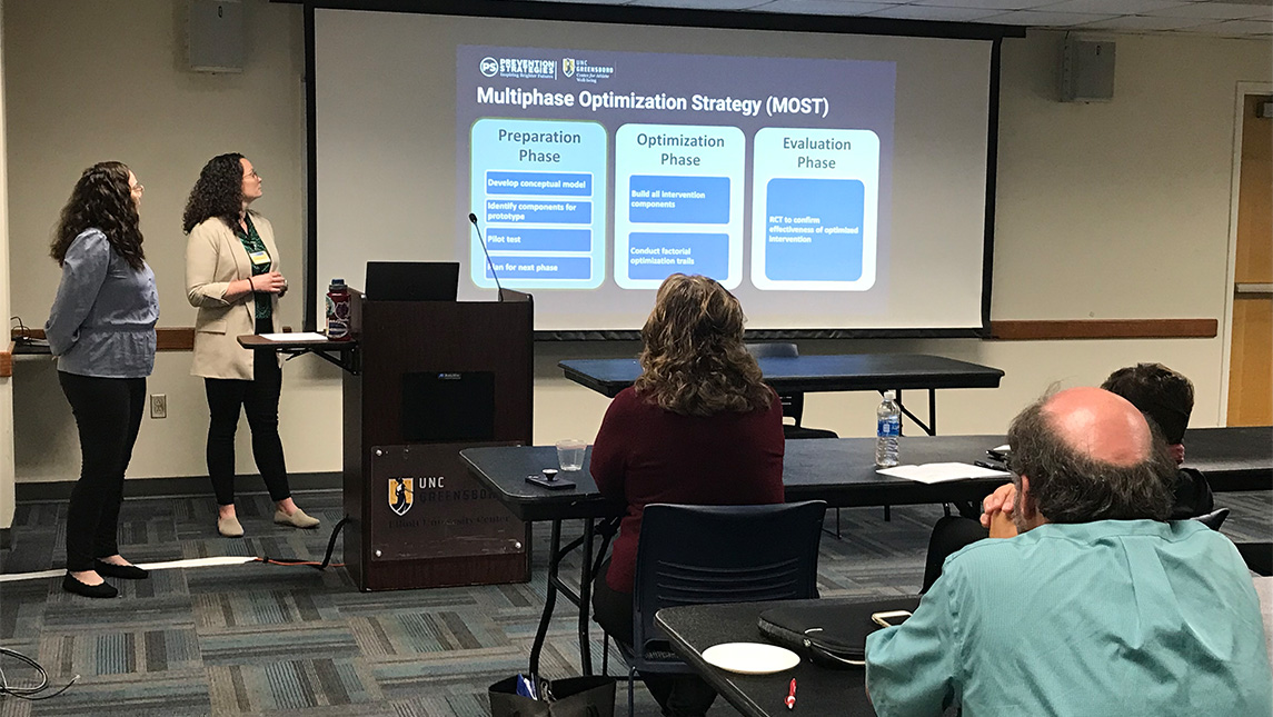 UNCG doctoral student Scarlett Ruppert gives a presentation with a projector at the front of a room.