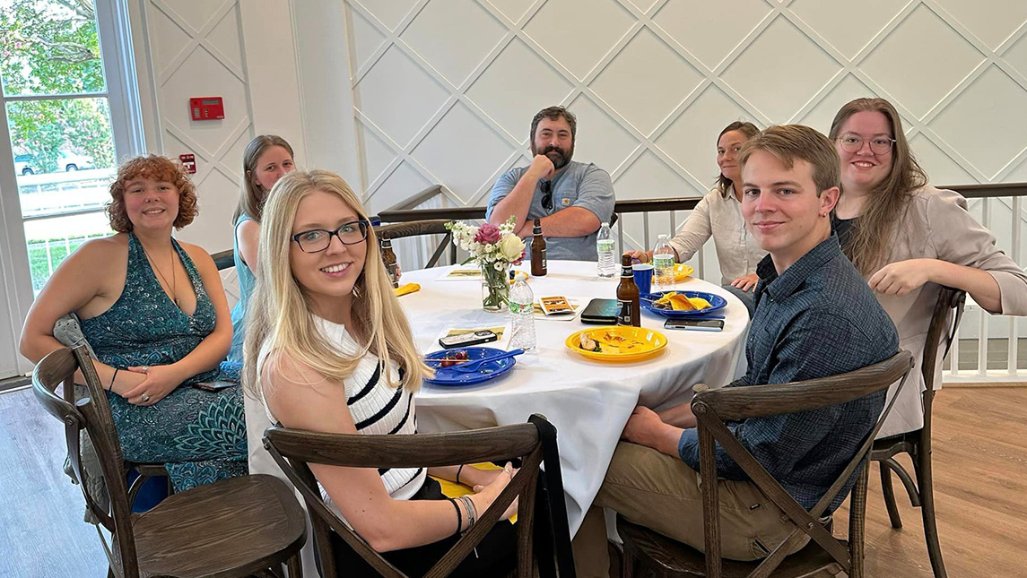 Conference participants smile while sitting at a lunch table.