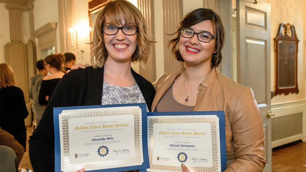 Amanda Wils and Allison Sermarini hold up their certificates for the UNCG Golden Chain Honor Society.