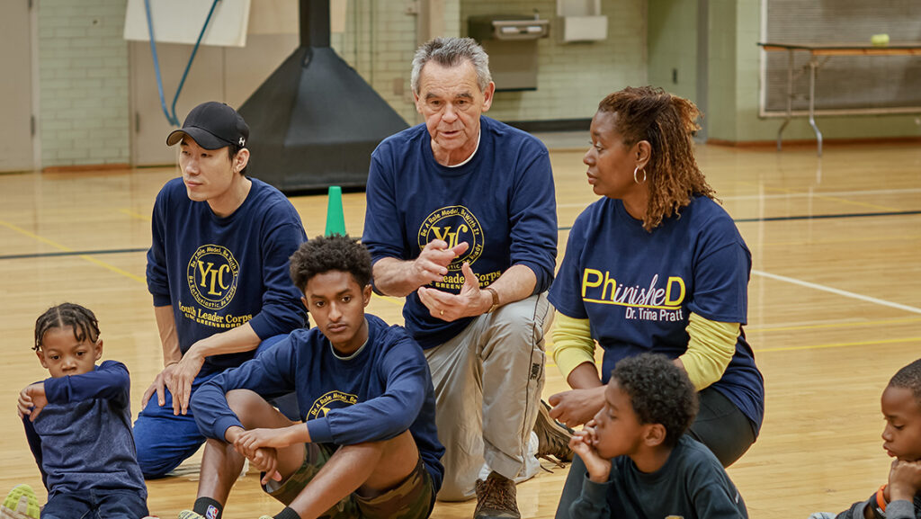 Retired UNCG Professor Tom Martinek with Dr. Trina Pratt work with kids on a basketball court.