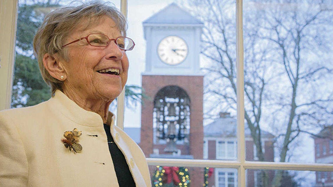 Dr. Nancy Vacc sits beside a window with the UNCG Vacc Clocktower outside.