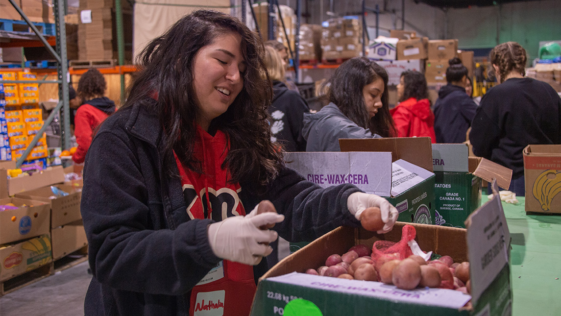 A UNCG student places food inside a box in a warehouse.