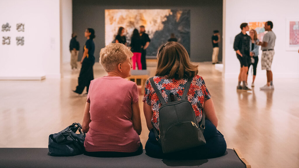 Two people sit on a bench inside the UNCG Weatherspoon Art Museum.