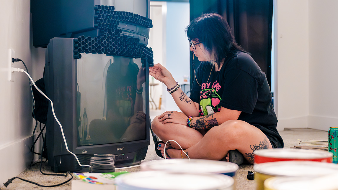 UNCG alum Ashe Smith works on an art piece involving two TVs in Greensboro Project Space