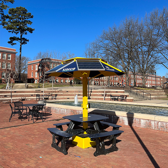 Picnic tables on the brick walk outside of Moran Commons beside fountains with campus buildings in the background.