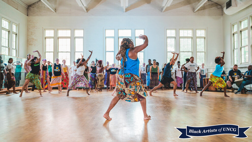 UNCG professor Robin Gee dances with her back turned to camera. A group of people dancers in front of her.