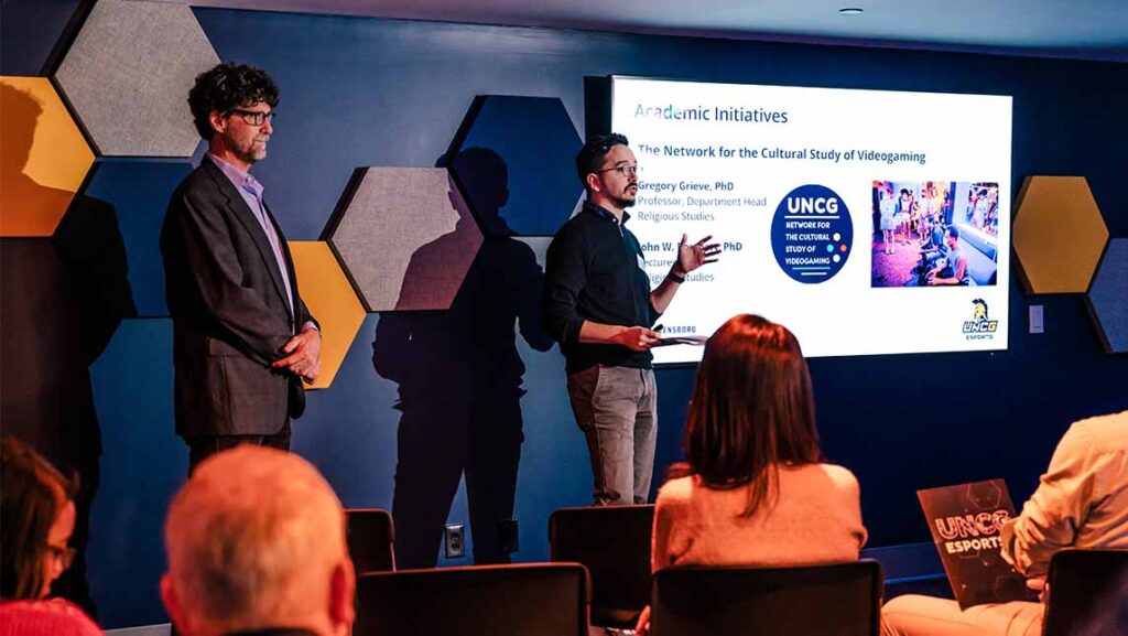 2 professors make a presentation about esports academic endeavors to other adults in the esports arena.