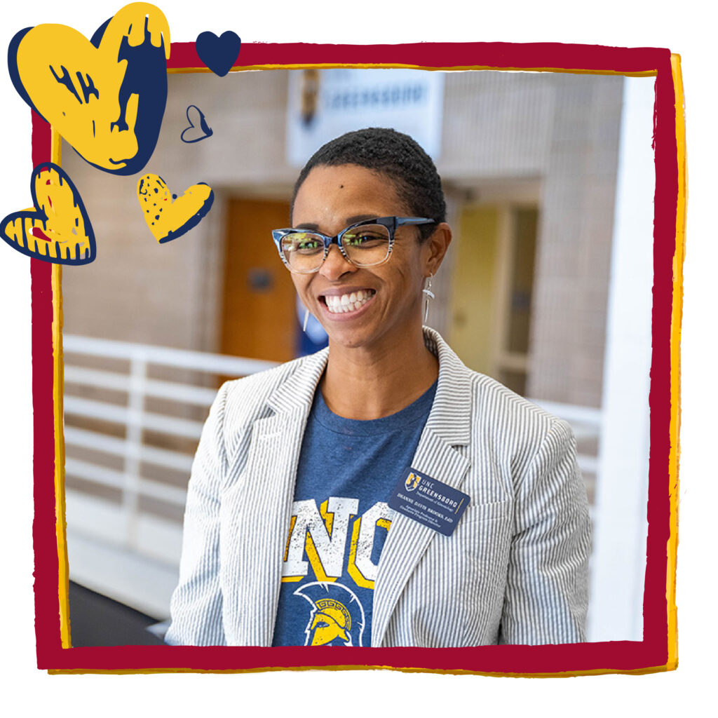 Woman in a UNCG t-shirt and a white lab coat poses for the camera. Red frame and blue and gold heart graphics have been added to headshot.