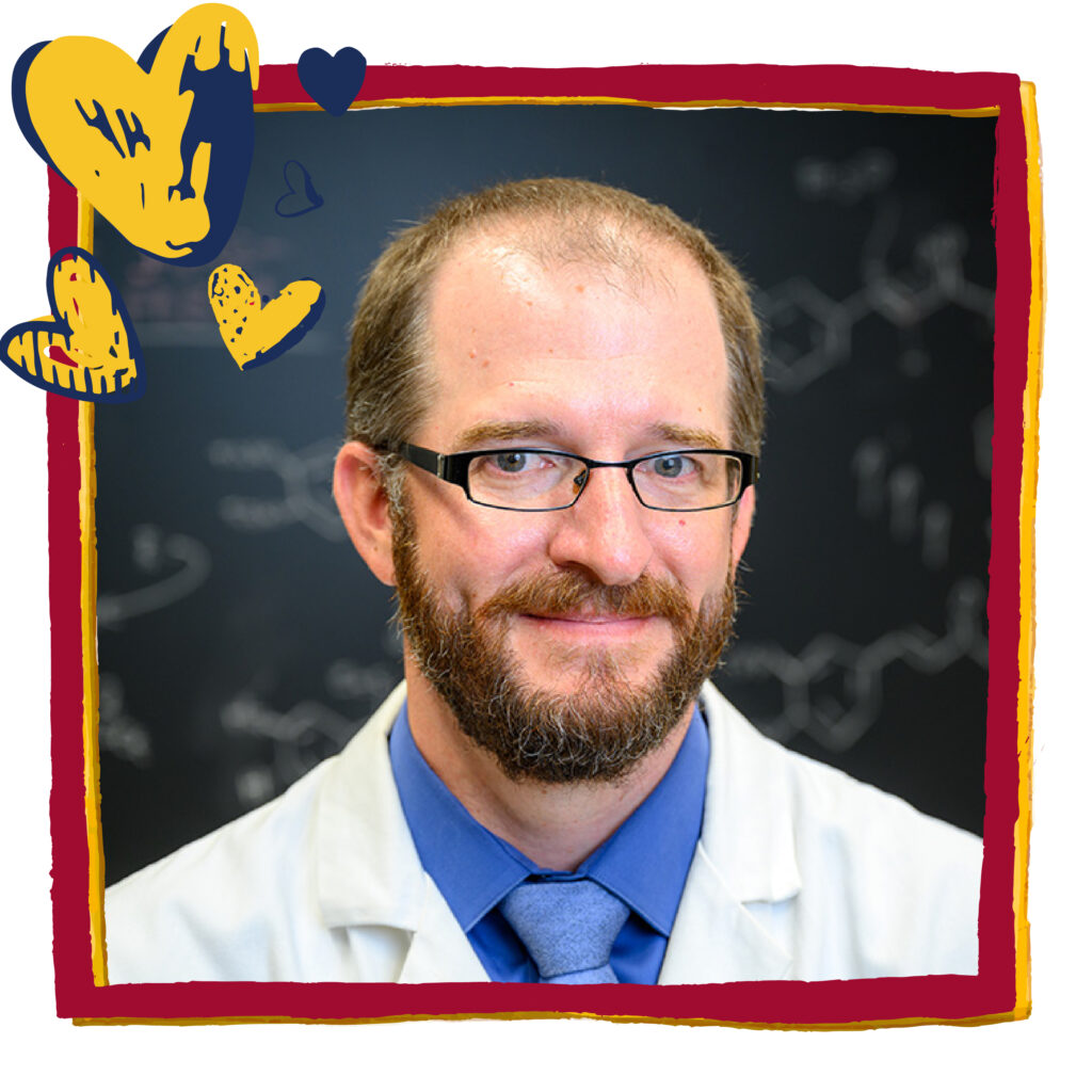 Man in a tie and a white lab coat poses in front of a blackboard with equations written on it. Red frame and blue and gold heart graphics have been added to headshot.
