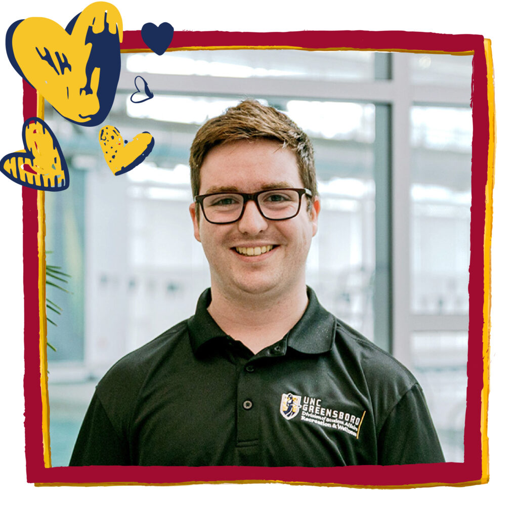 Man in a UNCG faculty polo smiles at the camera. Red frame and blue and gold heart graphics have been added to headshot.