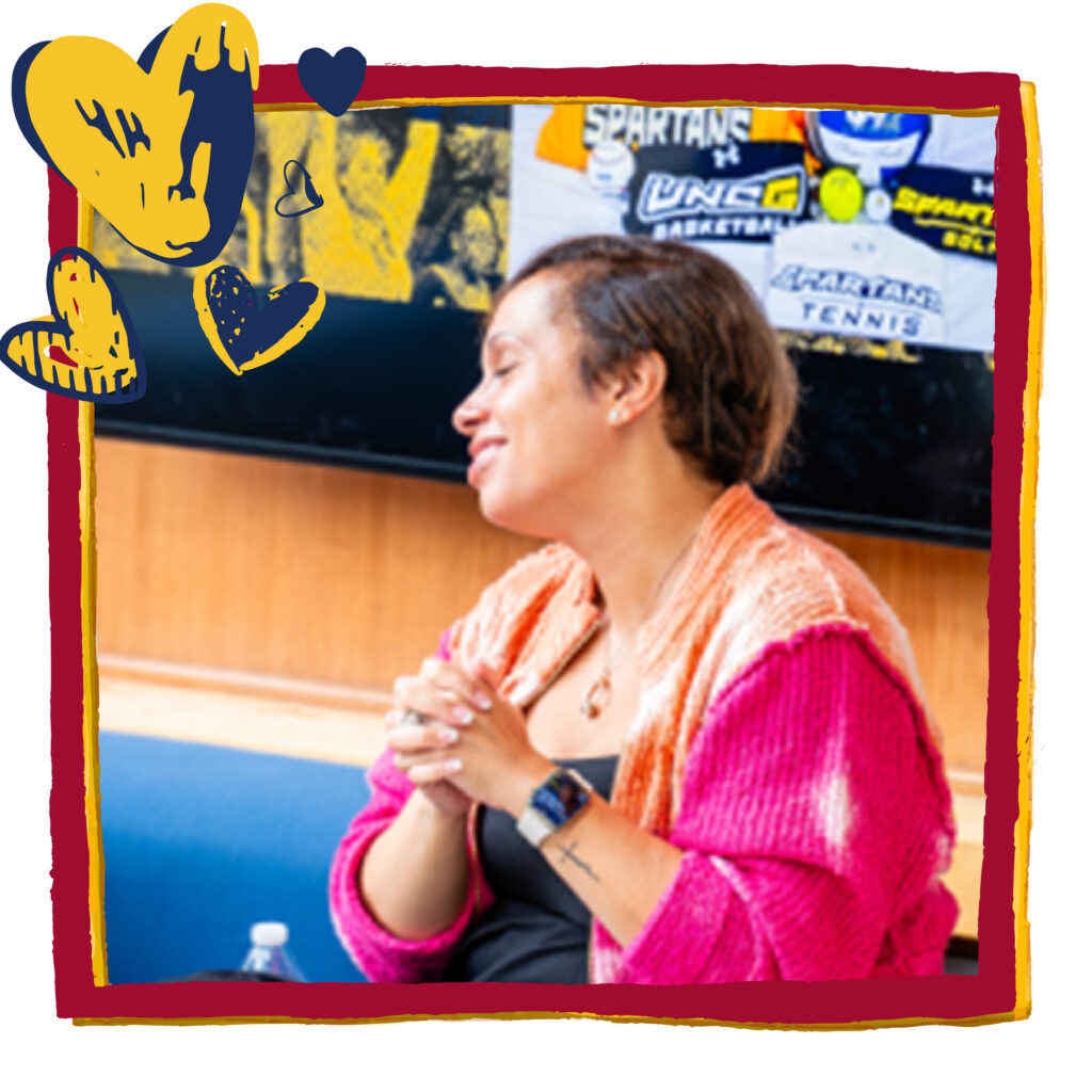 Woman sits on a bench looking away with her hands clasped. Red frame and blue and gold heart graphics have been added to headshot.